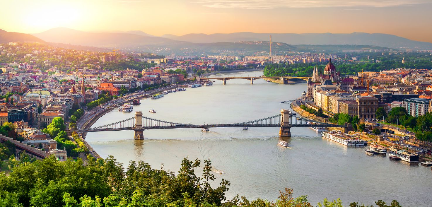 Photorealistic golden hour view of Budapest with the Hungarian Parliament building, Chain Bridge and Buda Castle reflected in the Danube River, showcasing the city’s iconic skyline.