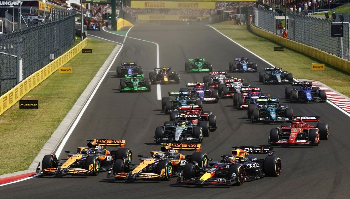 Aerial view of Formula 1 cars racing around the Hungaroring circuit during the Hungarian Grand Prix, with grandstands full of fans and the twisting track visible in the hills near Budapest.